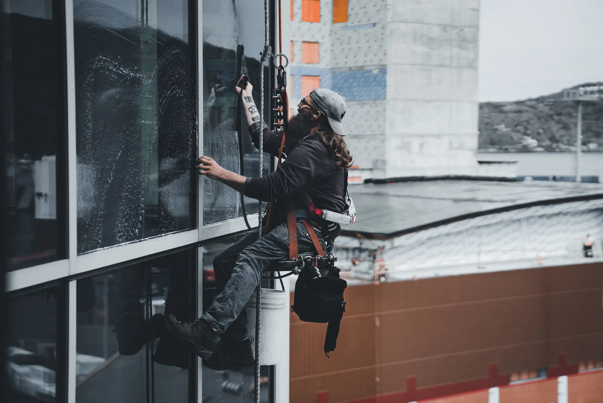 Window cleaner on ropes washing the glass facade of a commercial building