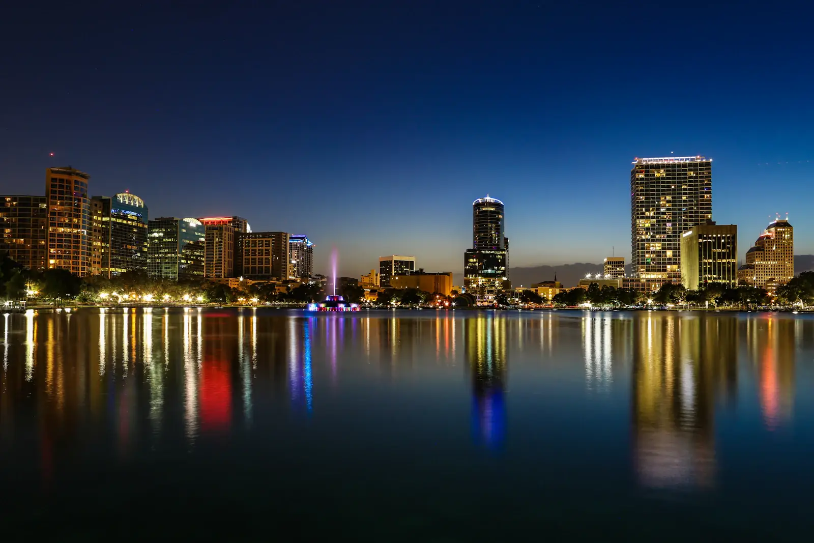 Downtown Orlando skyline lit up at night, reflected in Lake Eola
