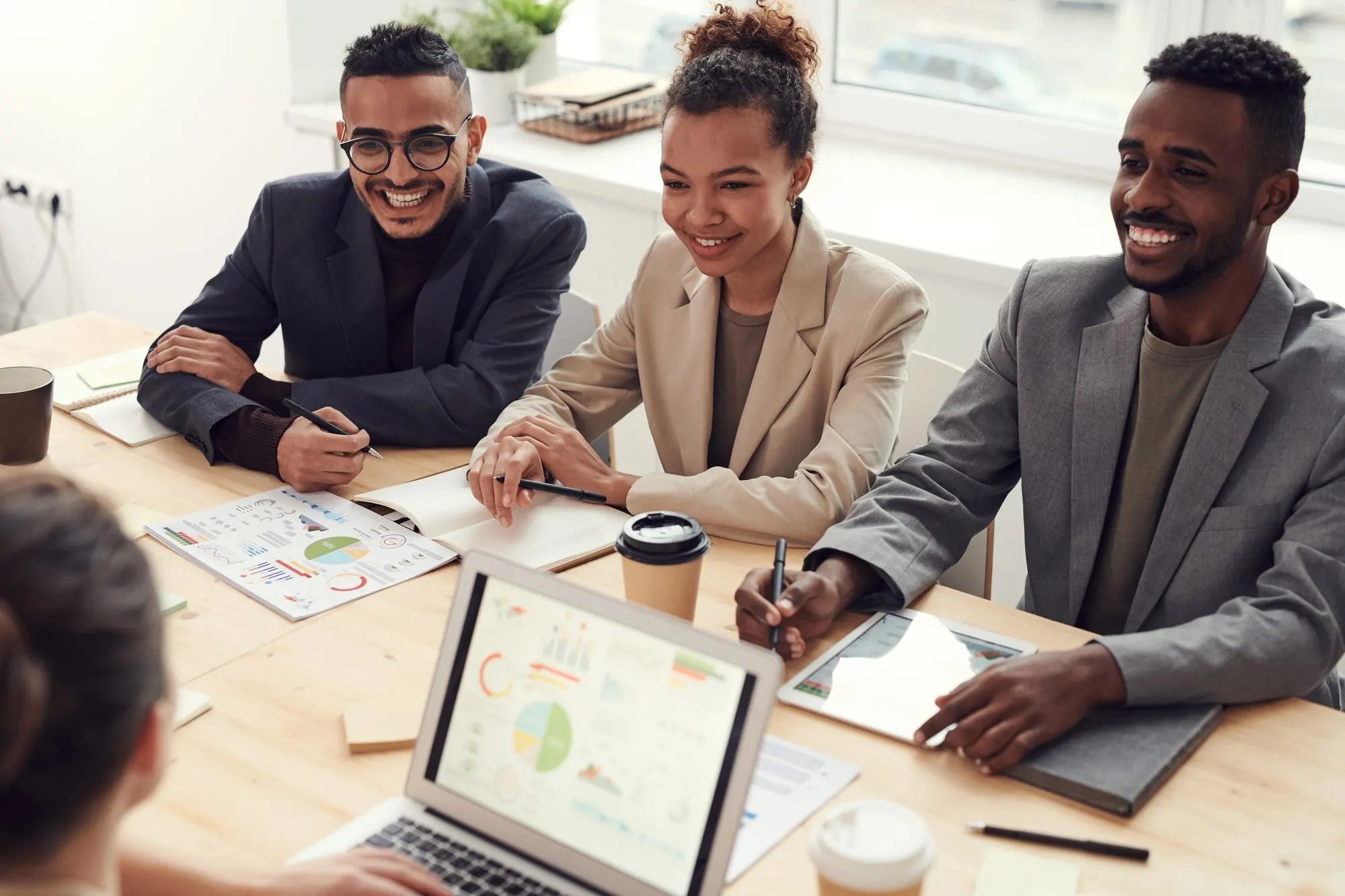 Three colleagues laughing together around a meeting table with laptops and charts