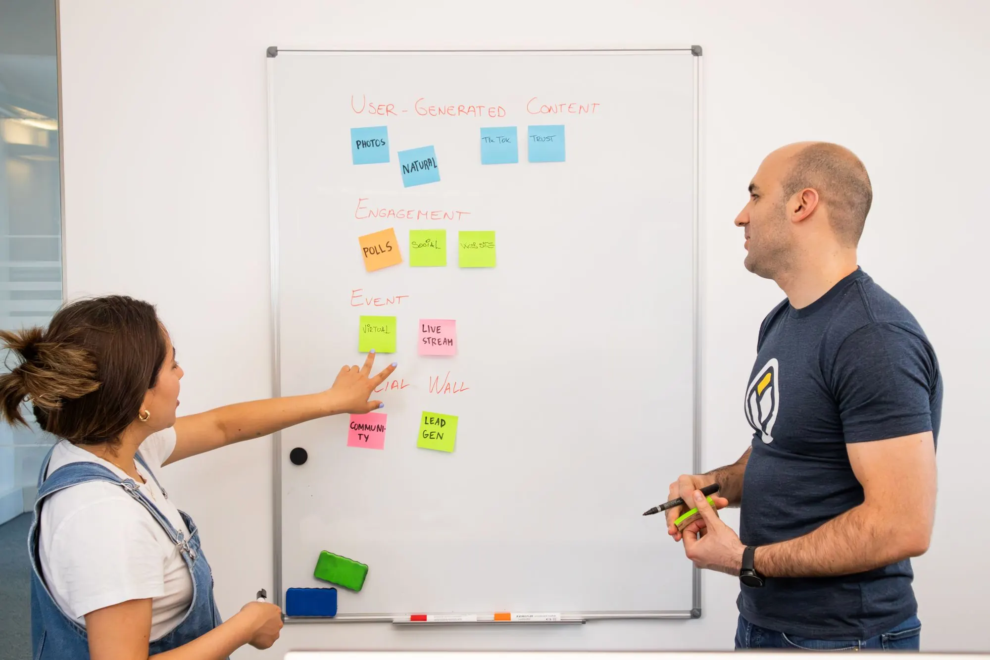 Two colleagues planning at a whiteboard covered in sticky notes