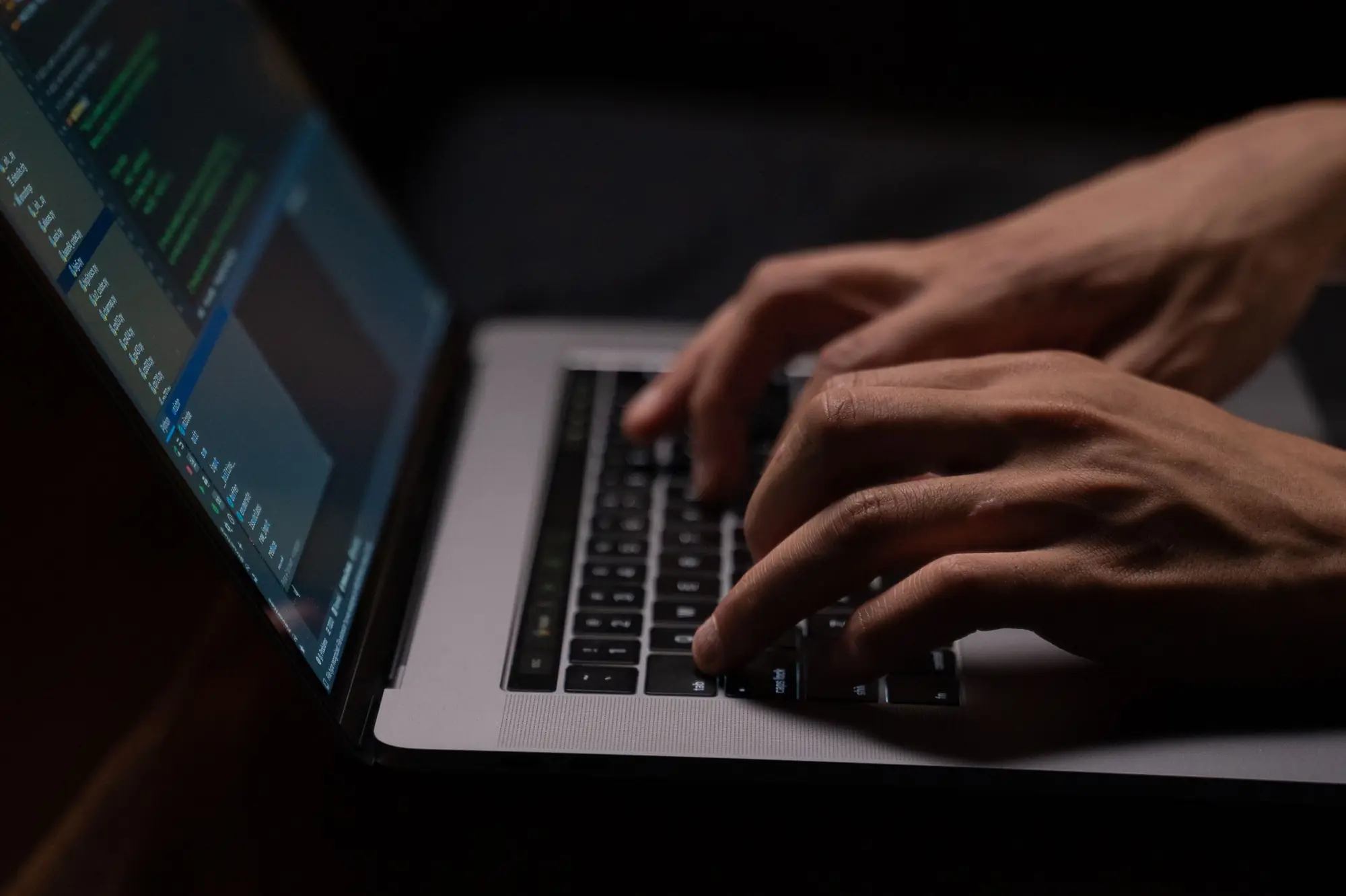 Hands typing on a laptop in a dark room