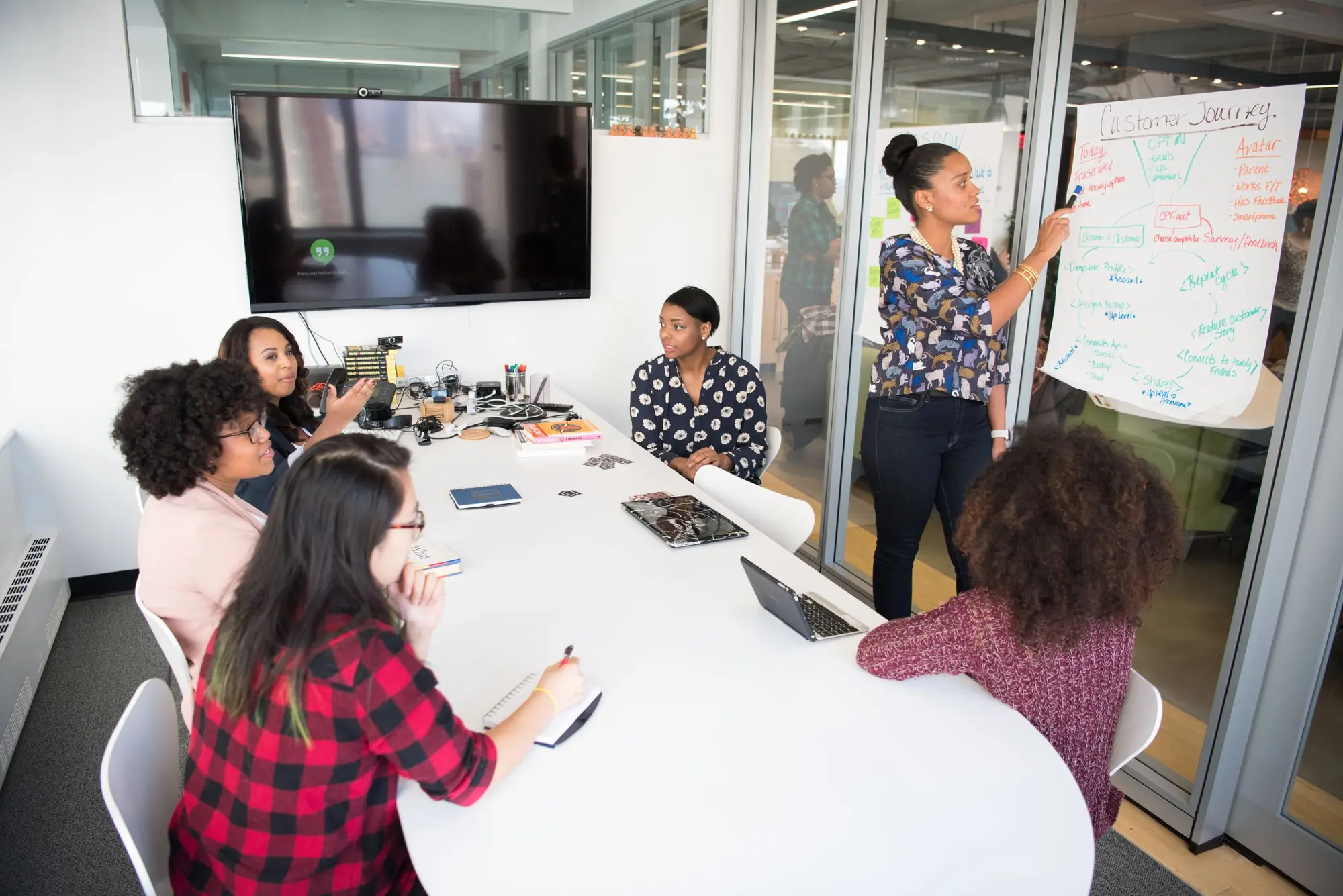 Team of women collaborating around a conference table with laptops and a whiteboard